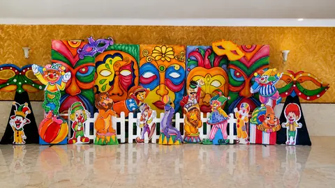 A carnival-themed party backdrop with cut-out masks and clown figures