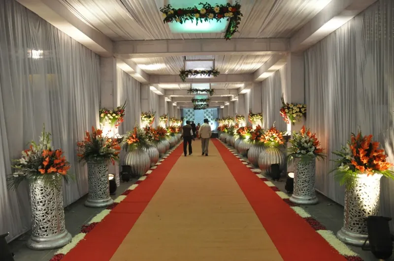 An ivory-draped wedding corridor with floral pillars running down a red and gold aisle