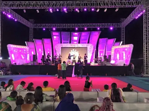 A large outdoor event stage under truss lighting in a magenta wash, with an audience watching